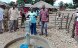 Eine Dorfbewohnerin in der Provinz Niassa im Norden Mosambiks betätigt eine neue Handpumpe. Um sie herum steht eine Gruppe weiterer Personen.