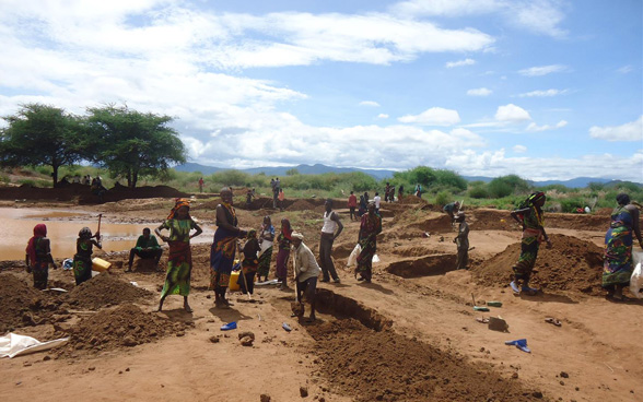 A group of Ethiopian men and women beside a half dried-up pool of water, using picks and shovels to dig new basins.