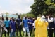 a group of health workers listen to the trainer's instructions, assisted by two individuals wearing protective clothing.   