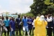 a group of health workers listen to the trainer's instructions, assisted by two individuals wearing protective clothing.