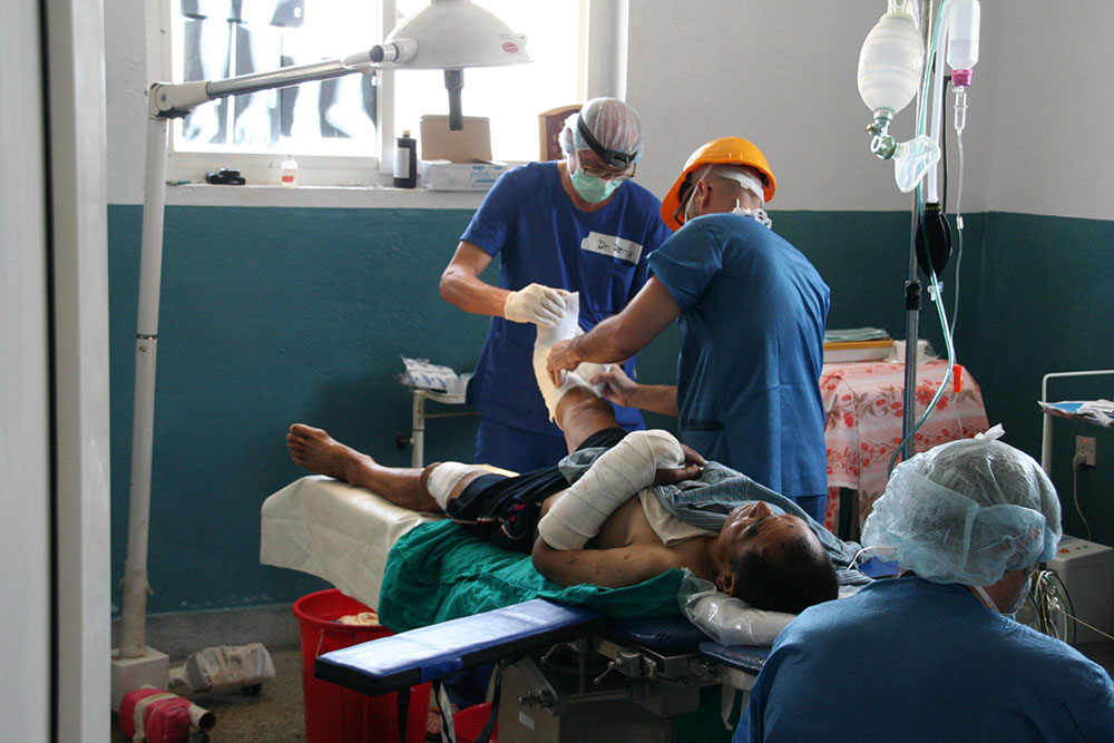 Three doctors operating on an injured patient's leg.  