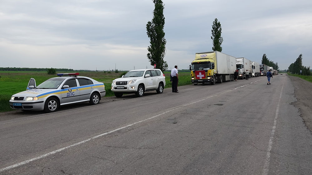Lorries displaying Swiss flags, driving along a road in Ukraine.