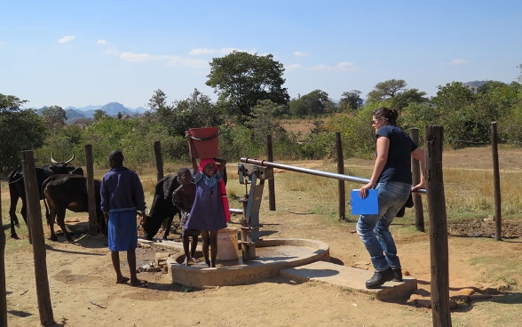 Children gather round an SHA expert as she pumps water from a well.