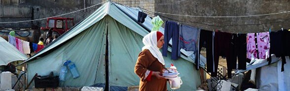A woman refugee walks in front of a tent.