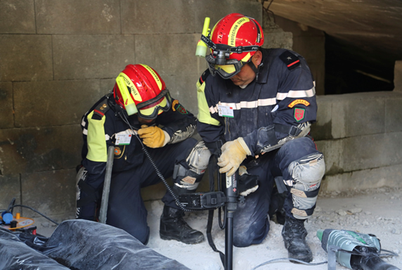 Two rescue workers training inside a destroyed building with a search device. 