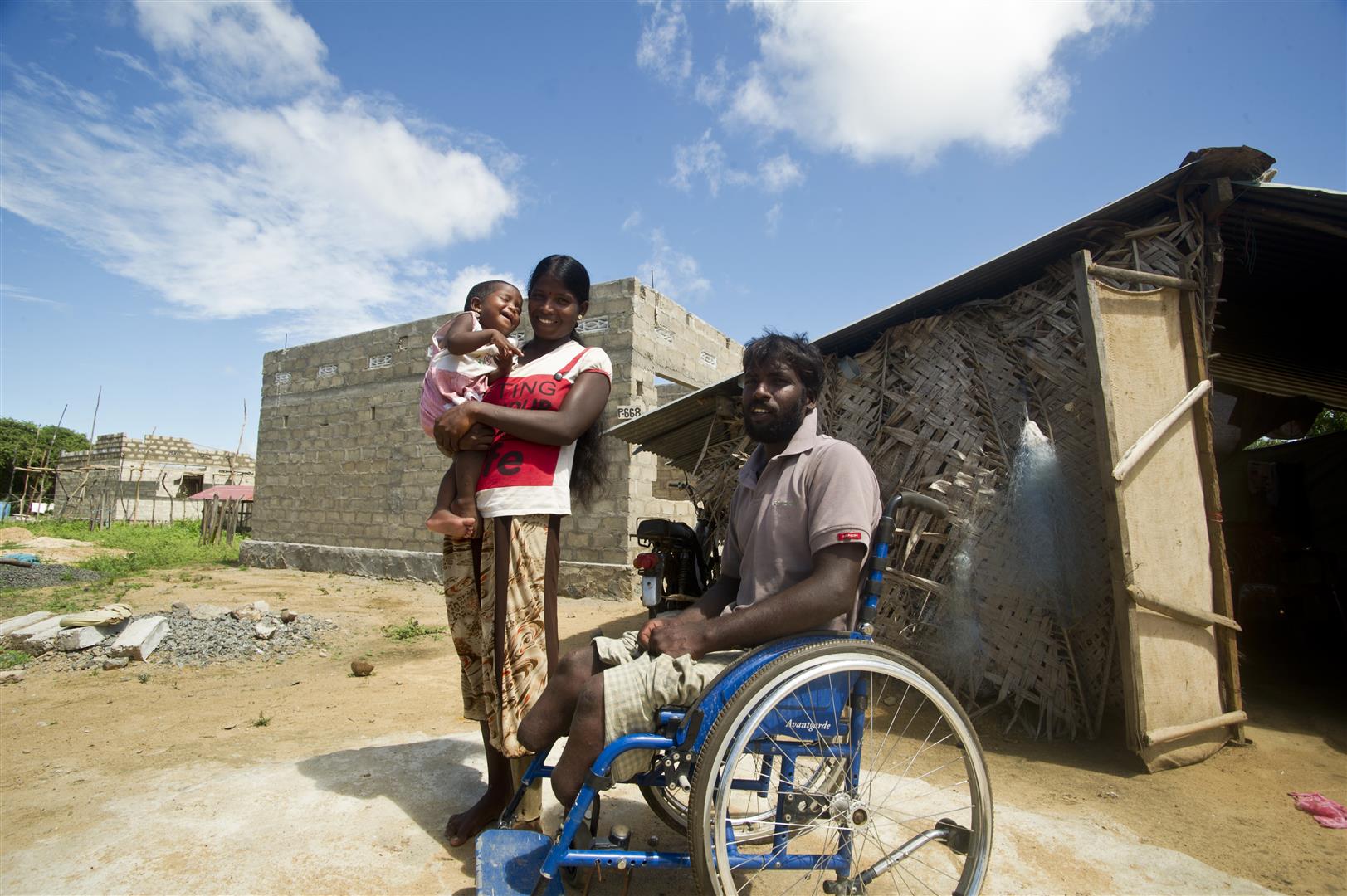 Un homme en chaise-roulante, son épouse et leur bébé posent devant leur future maison.