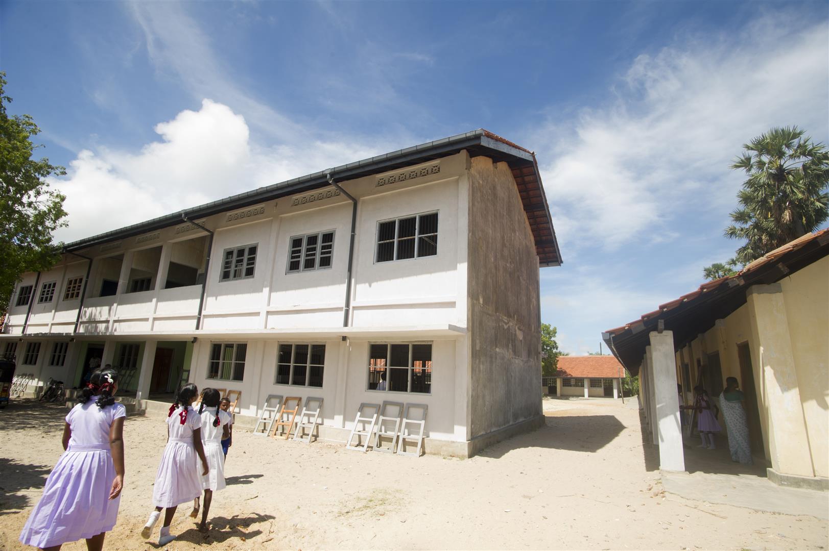 Trois écolières marchent vers leur école construites sur deux étages.