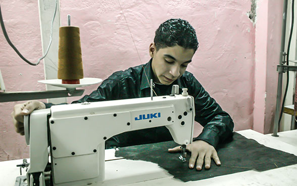 Un apprenti coud du tissu avec une machine à coudre