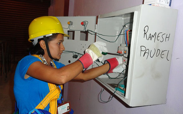 Une apprentie manipule un tournevis sur un panneau électrique