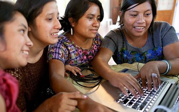 Cuatro mujeres están sentadas y trabajan alegremente delante un portátil. 