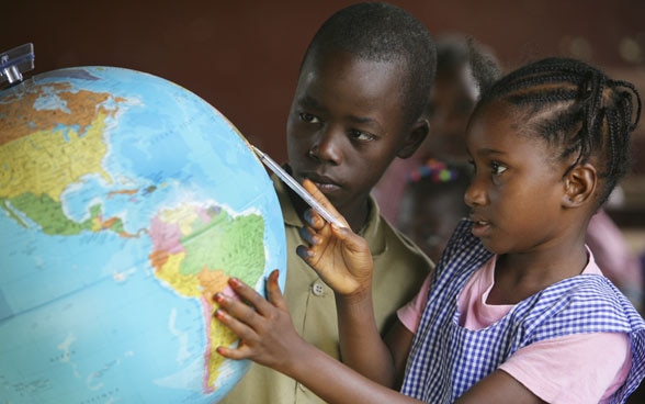 Kinder schauen sich in einem Klassenzimmer einen Globus an.