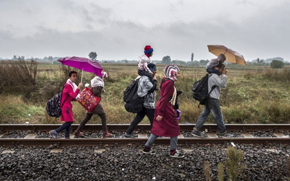 Flüchtlinge gehen im Regen Zugschienen entlang.
