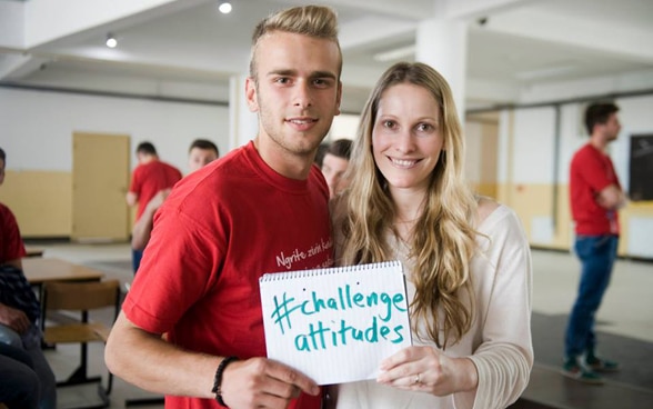 A young man and a young woman carry a poster saying ‘challenge attitudes’.