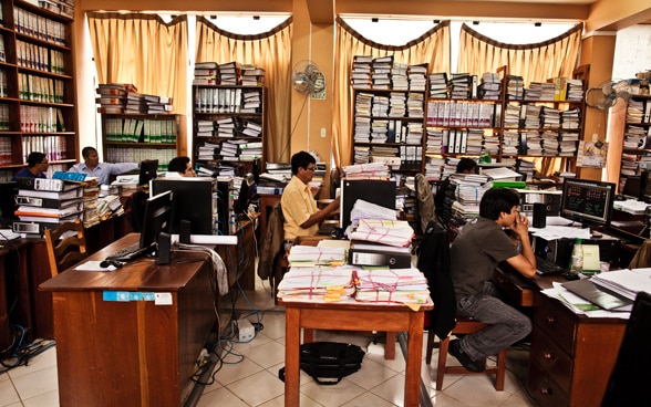 Angestellte in einem Büro voller Akten in Peru arbeiten am Computer.