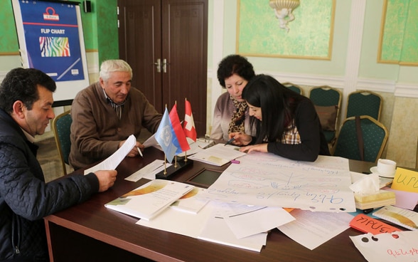 Two men and two women examine official documents in a meeting room in Armenia. 