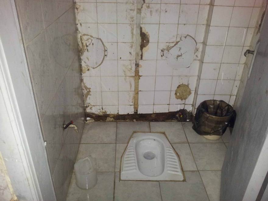 A toilet cubicle with damaged tile walls.