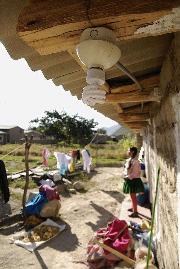 Una lampada a basso consumo elettrico appesa al tetto di una casa. Sullo sfondo si vede una bambina.