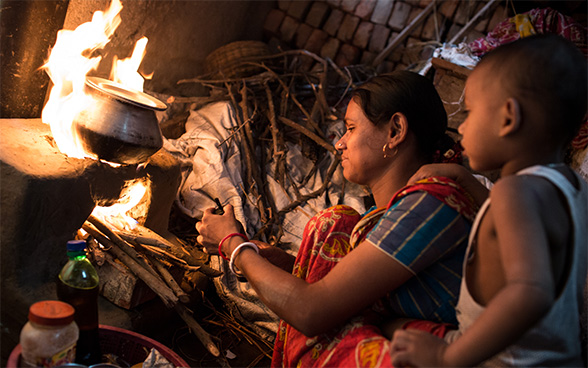 Una donna indiana prepara da mangiare in cucina; al suo fianco un bambino. 