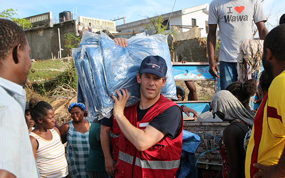 A Swiss expert surrounded by Haitians hands out tarpaulin sheets.