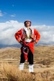 Ein nach peruanischer Tradition gekleideter Mann steht auf offenem Gelände im peruanischen Hochland und schaut in den Himmel.