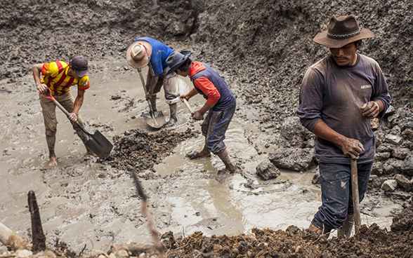 Quatre hommes munis de bêches s'affairent sur une source.