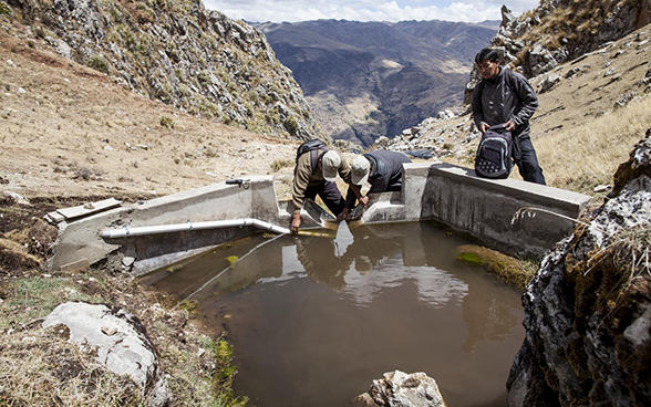 Trois hommes se tiennent près d'un réservoir d'eau.