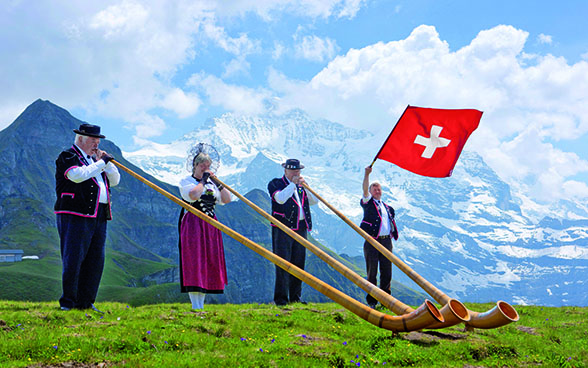 Des joueurs de cor des Alpes et un lanceur de drapeau devant le massif de la Jungfrau.