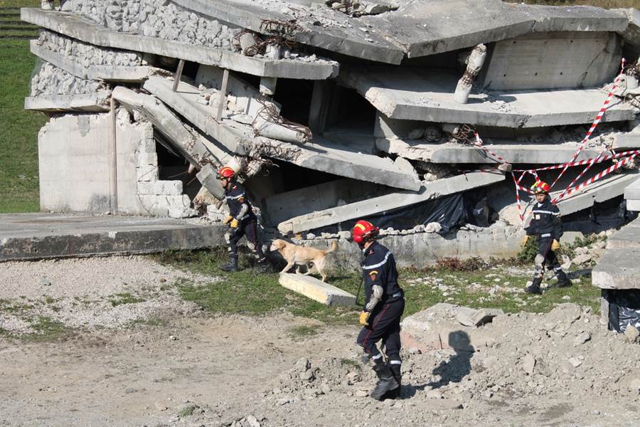 Tres socorristas marroquíes y un perro frente a un edificio en ruinas. 