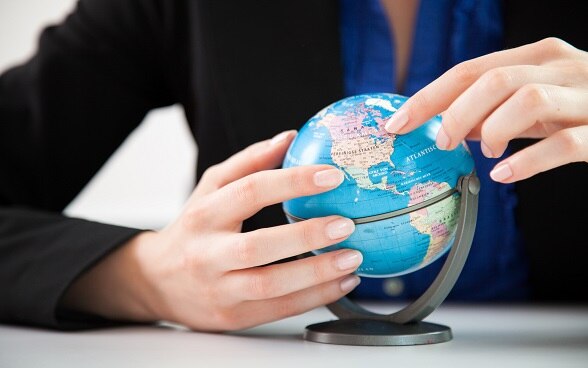 Two hands holding a small globe.