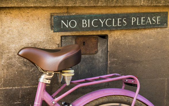 A pink bike against a wall with a sign reading ‘No bicycles please’ in capital letters.