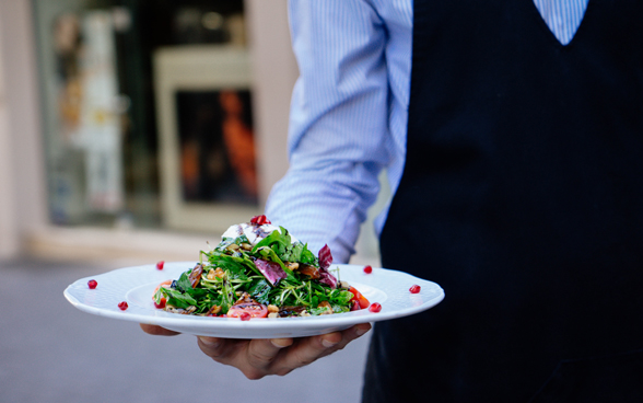 Ein Mann in einem gestreiften Hemd und Schürze serviert einen bunten Salat.