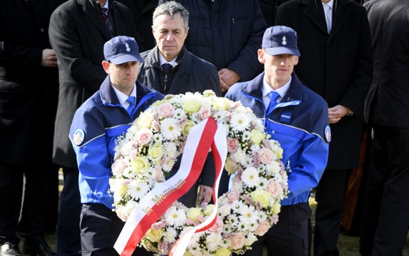 Ignazio Cassis è in piedi dietro a una corona di fiori. 