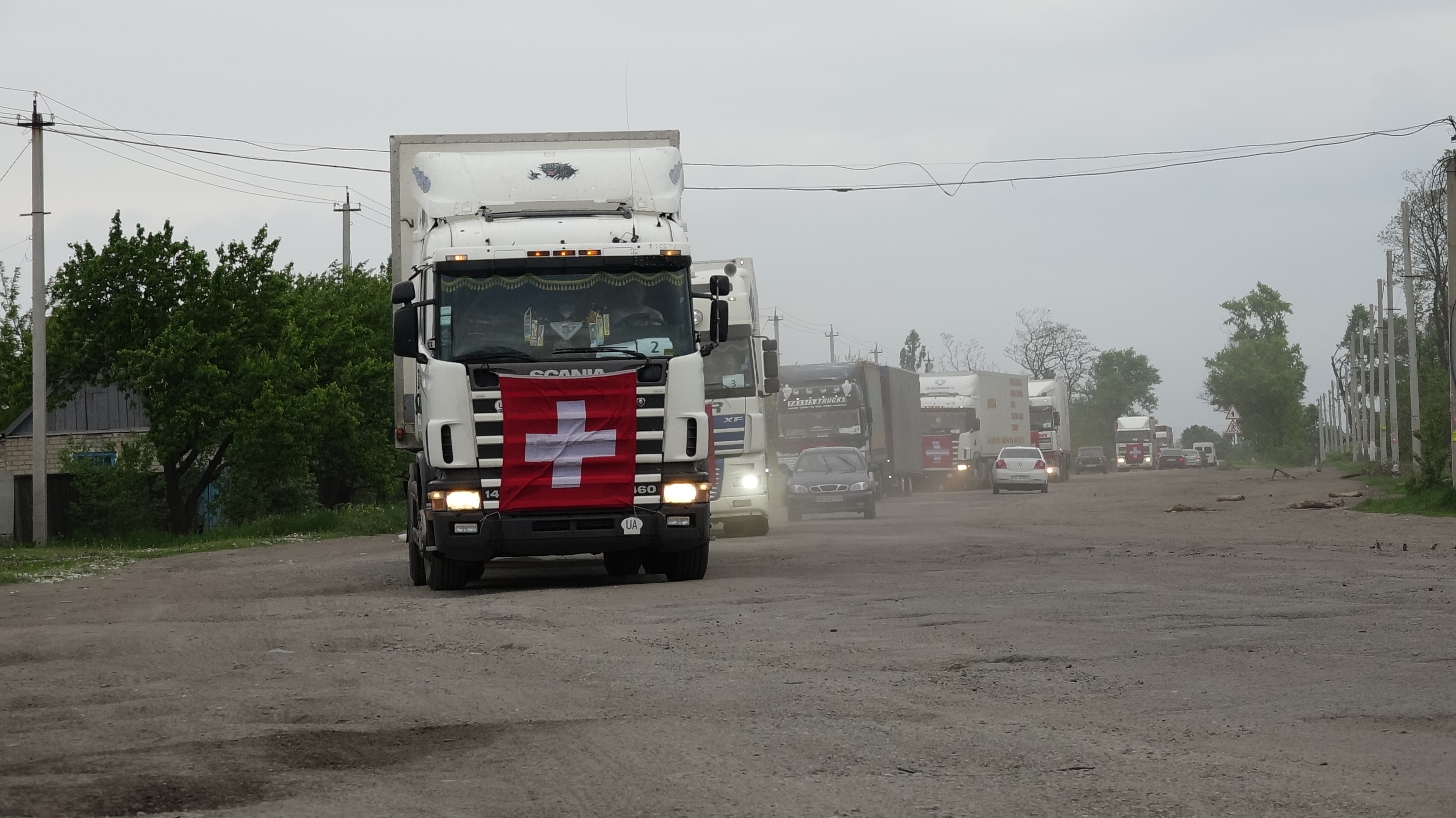 Des camions avec les drapeaux suisses circulent sur une route.  