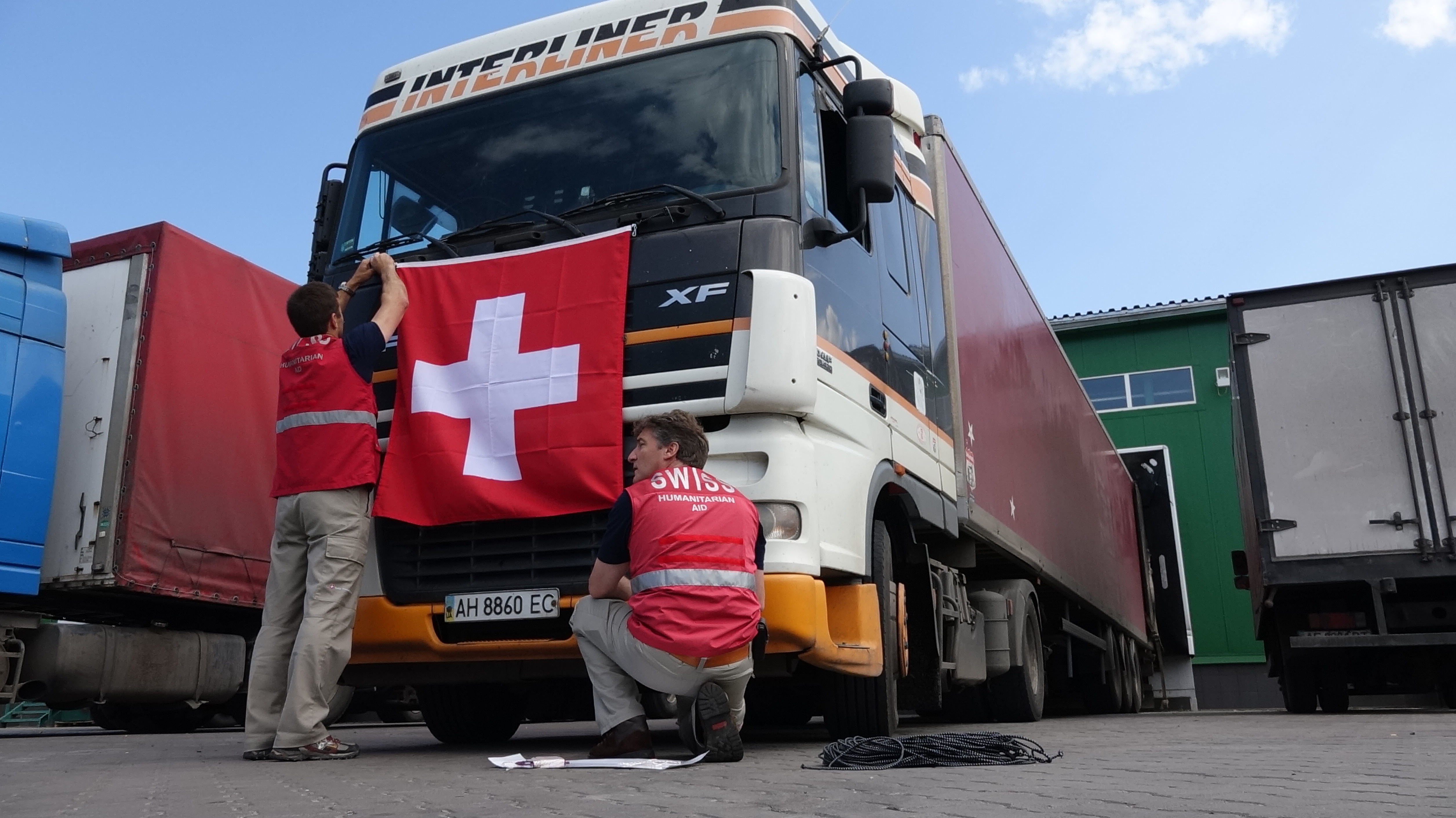 Due membri del Corpo svizzero di Aiuto umanitario attaccano la bandiera svizzera al cofano di un camion. 