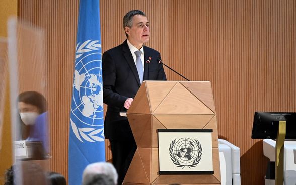 Bundespräsident Cassis steht an einem Pult und spricht. Neben ihm steht eine Flagge der UNO.