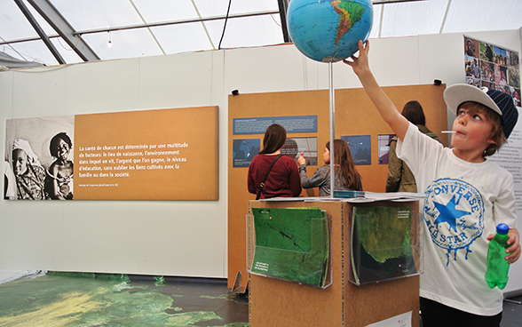 In primo piano, un bambino studia un mappamondo nello stand della DSC. © DFAE