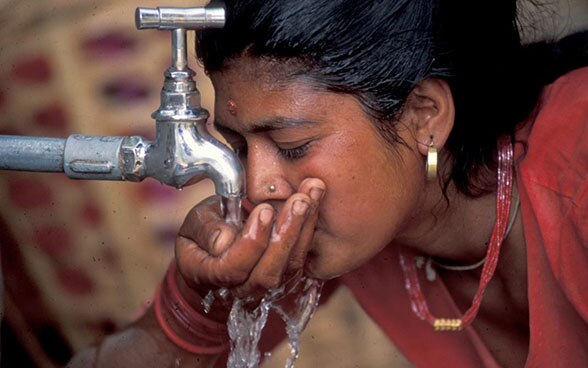 Frau trinkt Wasser von einem Wasserhahn.