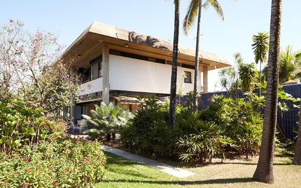Vue du bâtiment de deux étages, avec des arbustes et des palmiers au premier plan.