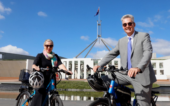 A woman and a man on e-bikes in front of a building.