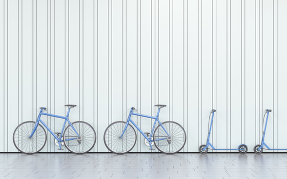 Bicycles and scooters leaning against a wall. 