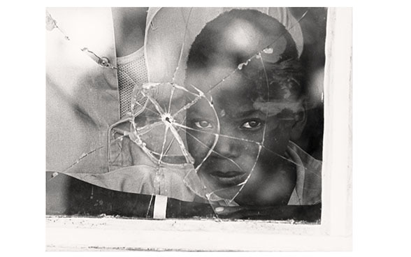 Ein Junge aus Mosambik schaut durch eine Scheibe mit Einschussloch