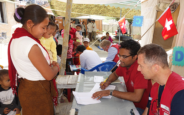 Swiss Humanitarian Aid employees explaining something written in a document to a local woman in Nepal.