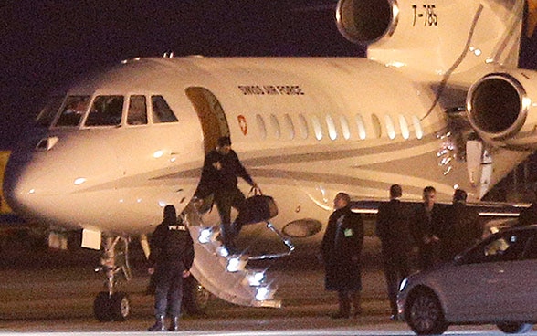 Un homme descend d’un avion des Forces aériennes suisses à Genève. Des agents de sécurité et d’autres personnes les y attendent.