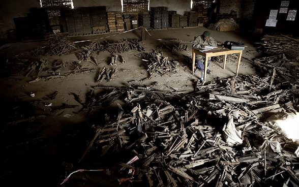 A congolese soldier counts the numerous weapons on the floor.