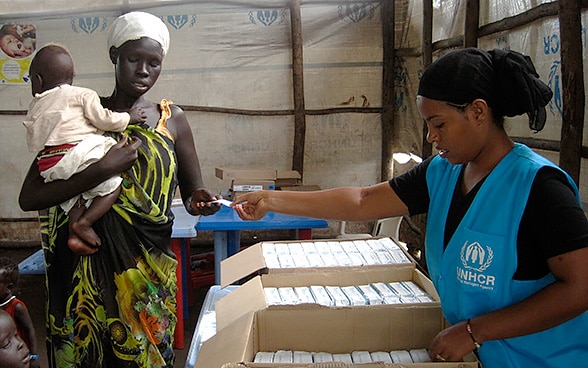 Eine Frau mit einem Kind erhält in einem Zelt der Vereinten Nationen einen Gutschein für Lebensmittel.