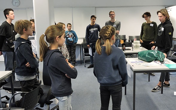 A group of children listen to FDFA employees describing their work.