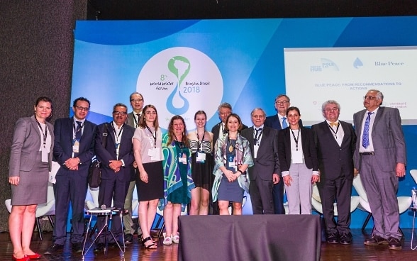 Six women and nine men of different nationalities in front of a blue wall with the logo of the World Water Forum in Brasilia.