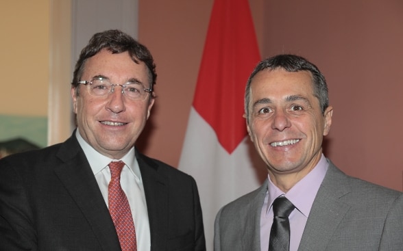 Ignazio Cassis and Achim Steiner standing, the swiss flag in the background.