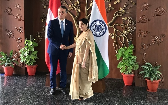 Le Conseiller fédéral Cassis serre la main de la Ministre indienne des affaires étrangères Sushma Swaraj. En arrière-plan se trouvent les drapeaux de l'Inde et de la Suisse.
