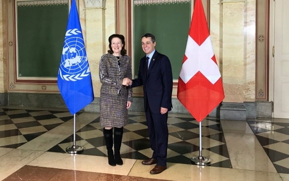 Il consigliere federale Cassis stringe la mano a Henrietta Fore. Sullo sfondo si vedono le bandiere della Svizzera e dell'ONU.